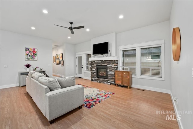 living room with a stone fireplace, light hardwood / wood-style flooring, and ceiling fan