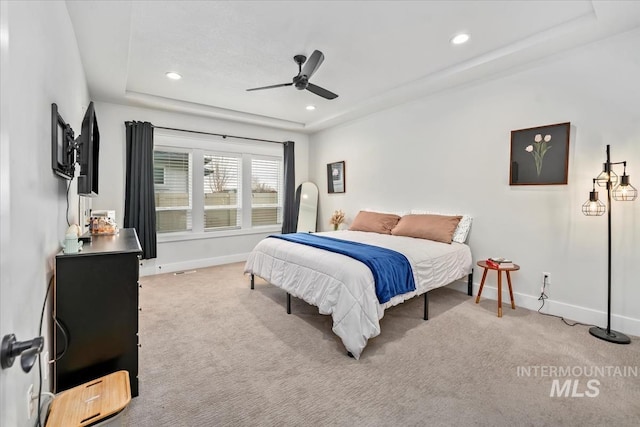 bedroom with ceiling fan, light colored carpet, and a raised ceiling