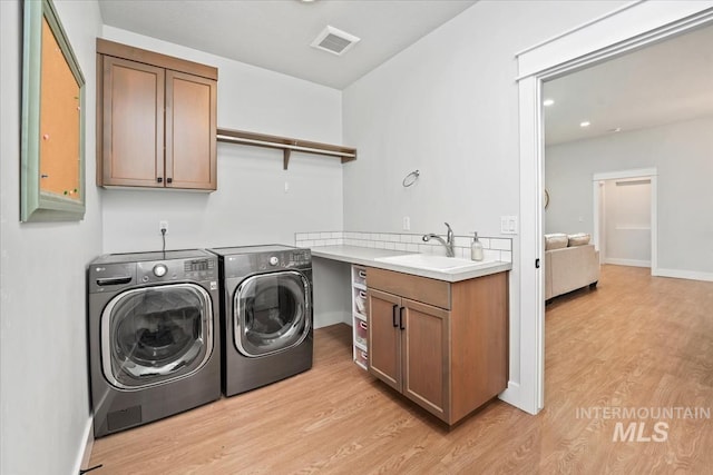 laundry room with cabinets, sink, washing machine and dryer, and light hardwood / wood-style flooring