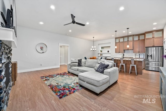 living room featuring a stone fireplace, ceiling fan with notable chandelier, and light wood-type flooring