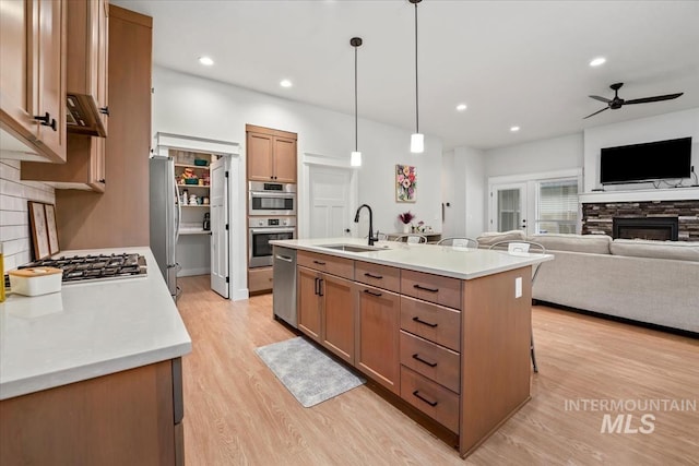 kitchen featuring sink, hanging light fixtures, stainless steel appliances, a fireplace, and a center island with sink