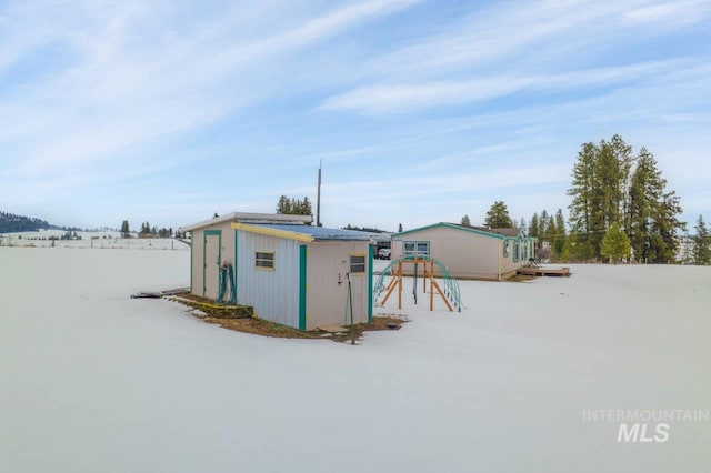 snow covered structure with a shed, a playground, and an outdoor structure