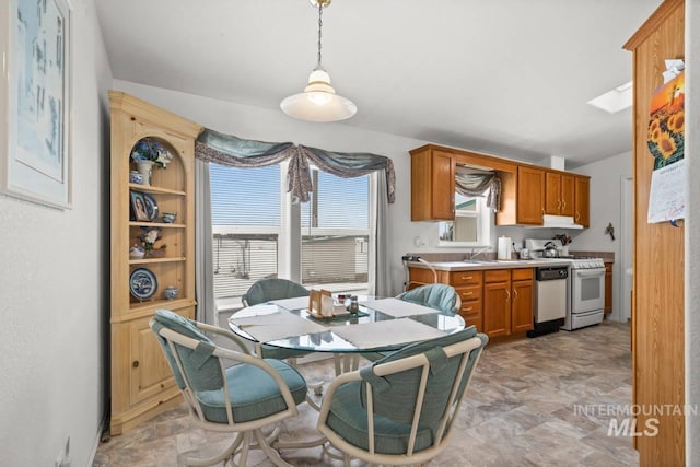 kitchen with white appliances, a skylight, hanging light fixtures, light countertops, and a sink