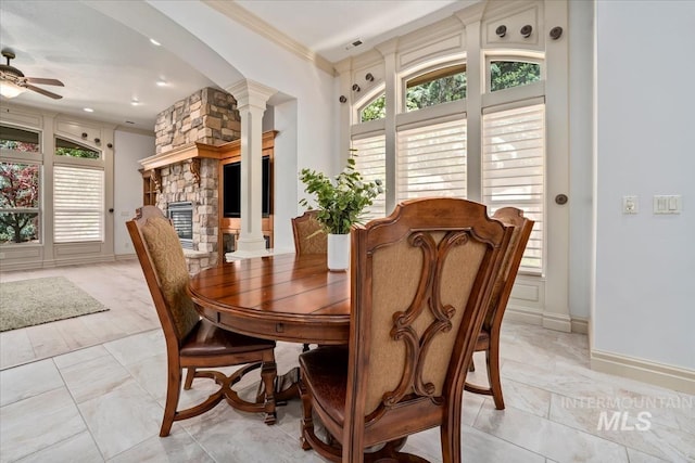 dining room with crown molding, decorative columns, a stone fireplace, and marble finish floor
