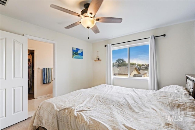 bedroom featuring a spacious closet, light colored carpet, and ceiling fan