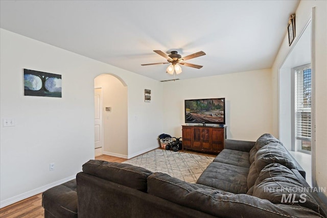 living room featuring baseboards, arched walkways, ceiling fan, and wood finished floors