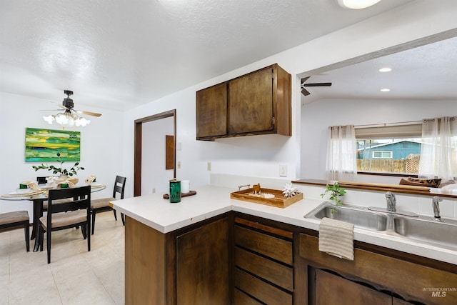 kitchen featuring ceiling fan, light countertops, a peninsula, light tile patterned flooring, and a sink