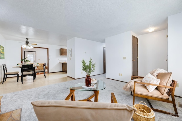 living area with a textured ceiling, light colored carpet, baseboards, and ceiling fan