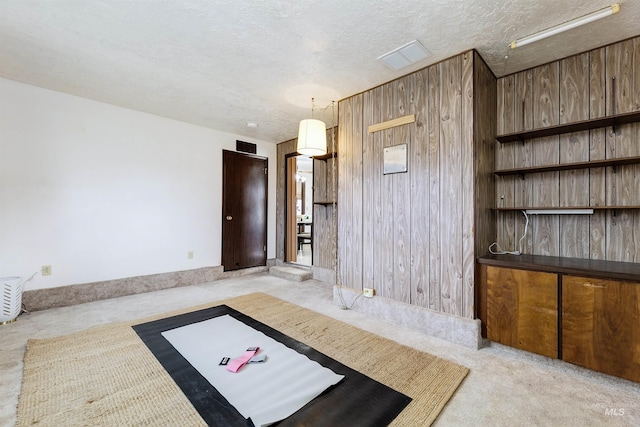 interior space with wooden walls, light colored carpet, and a textured ceiling