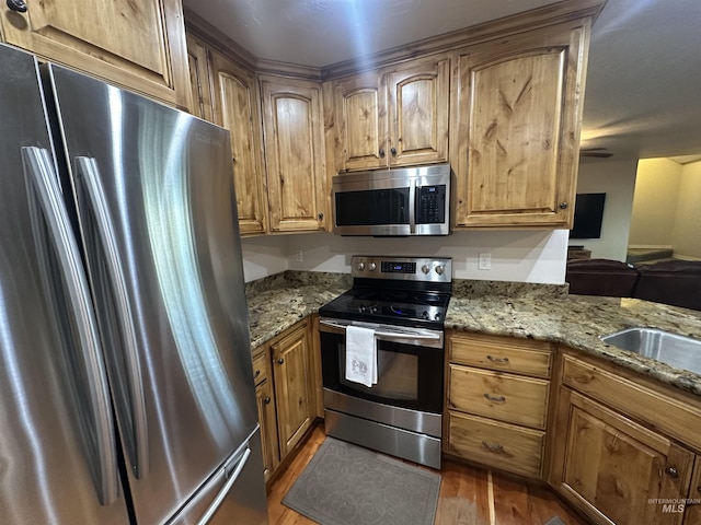 382 N 1020 E, Declo, ID 83323 - kitchen featuring brown cabinetry, appliances with stainless steel finishes, wood finished floors, a sink, and light stone counters