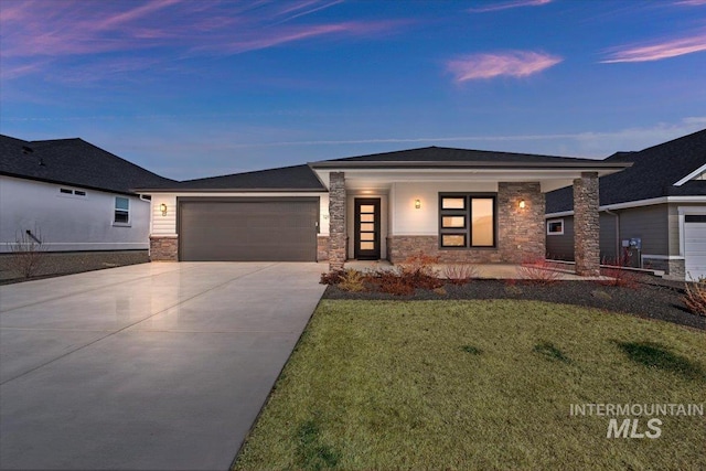 prairie-style house featuring stone siding, a lawn, concrete driveway, and a garage