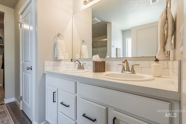 3772 S Walnut Ridge Way, Nampa, ID 83686 - bathroom featuring double vanity, decorative backsplash, a shower with shower door, a textured ceiling, and wood finished floors