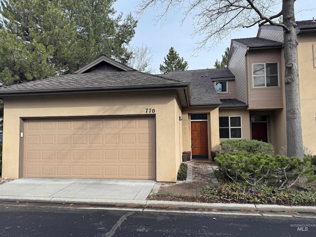 view of front of property with stucco siding, an attached garage, a shingled roof, and driveway