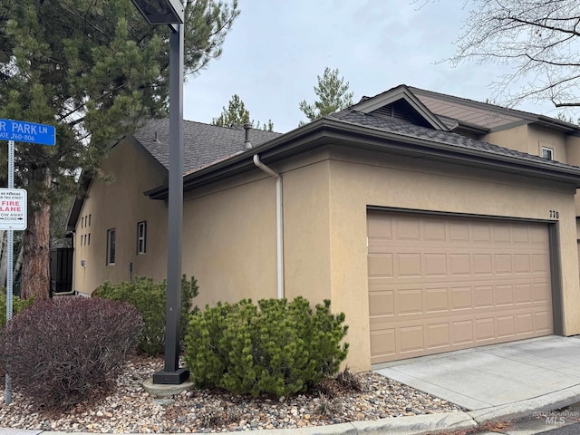 view of side of home featuring roof with shingles, a garage, driveway, and stucco siding