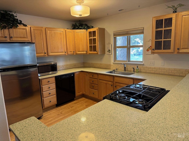 kitchen with light stone countertops, a sink, stainless steel appliances, glass insert cabinets, and light wood-type flooring