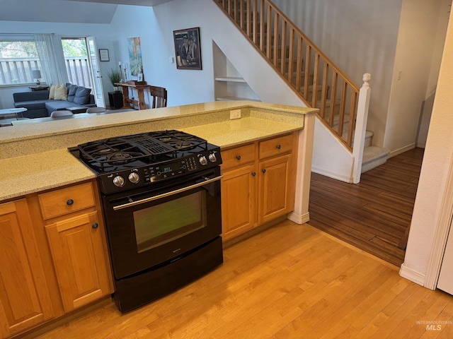 kitchen with baseboards, light stone countertops, open floor plan, light wood-style floors, and gas stove