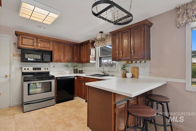 kitchen with a breakfast bar, decorative backsplash, a peninsula, black appliances, and a sink