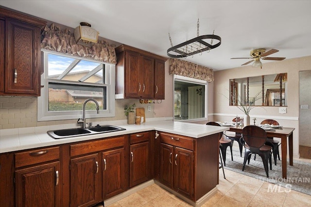 kitchen with a peninsula, ceiling fan, a sink, light countertops, and tasteful backsplash