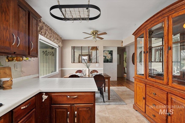 kitchen with tile countertops, glass insert cabinets, a peninsula, and ceiling fan with notable chandelier