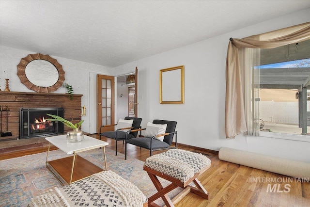 living area featuring a brick fireplace, wood finished floors, baseboards, and a textured ceiling