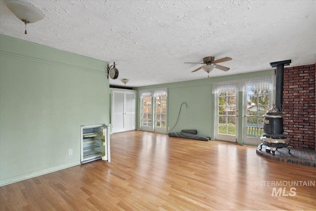 unfurnished living room with light wood-style floors, a textured ceiling, a wood stove, and a ceiling fan