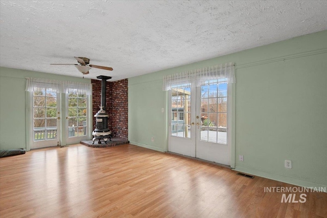 unfurnished living room featuring a wealth of natural light, visible vents, wood finished floors, and a wood stove