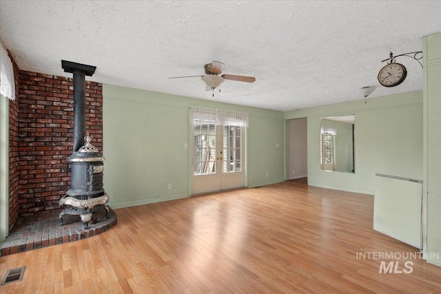 unfurnished living room with visible vents, a textured ceiling, wood finished floors, ceiling fan, and a wood stove