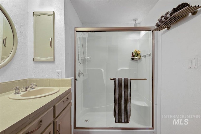 full bathroom with a stall shower, vanity, and a textured wall