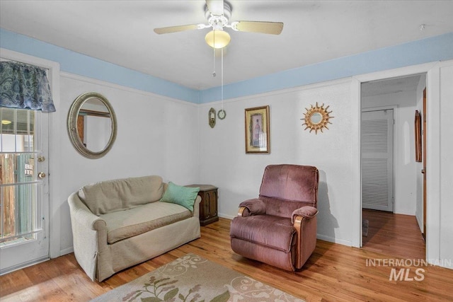 living area featuring baseboards, a ceiling fan, and wood finished floors