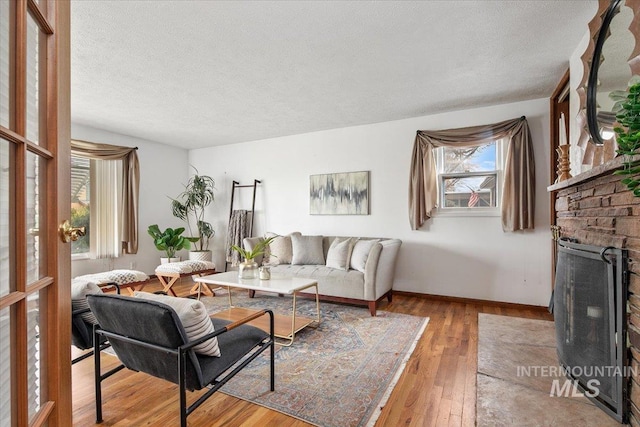 living room featuring baseboards, light wood-style floors, a brick fireplace, and a textured ceiling