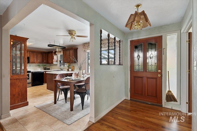 entryway featuring ceiling fan with notable chandelier, light wood-style floors, and baseboards