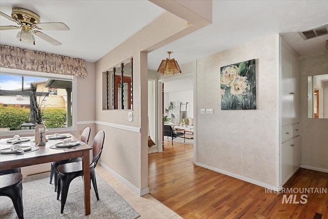 dining room featuring light wood-style flooring, a textured wall, visible vents, and ceiling fan