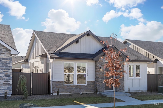 view of front of house with board and batten siding, stone siding, roof with shingles, and fence