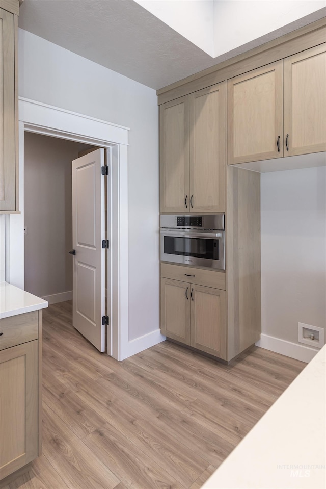 kitchen with light wood-style floors, light brown cabinets, stainless steel oven, and light countertops