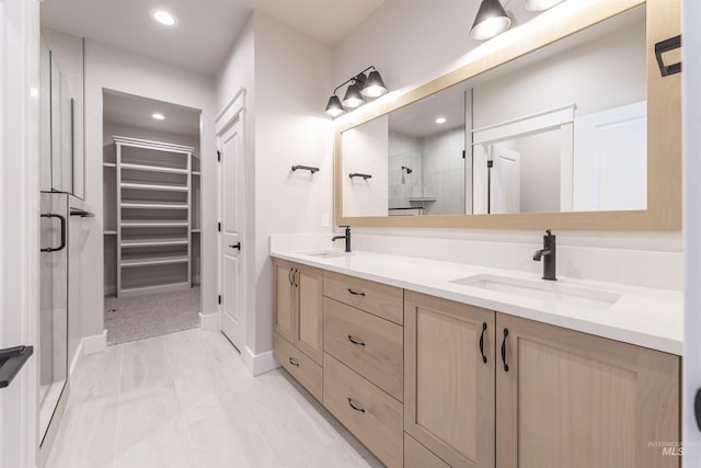 full bathroom with a spacious closet, double vanity, a stall shower, and a sink