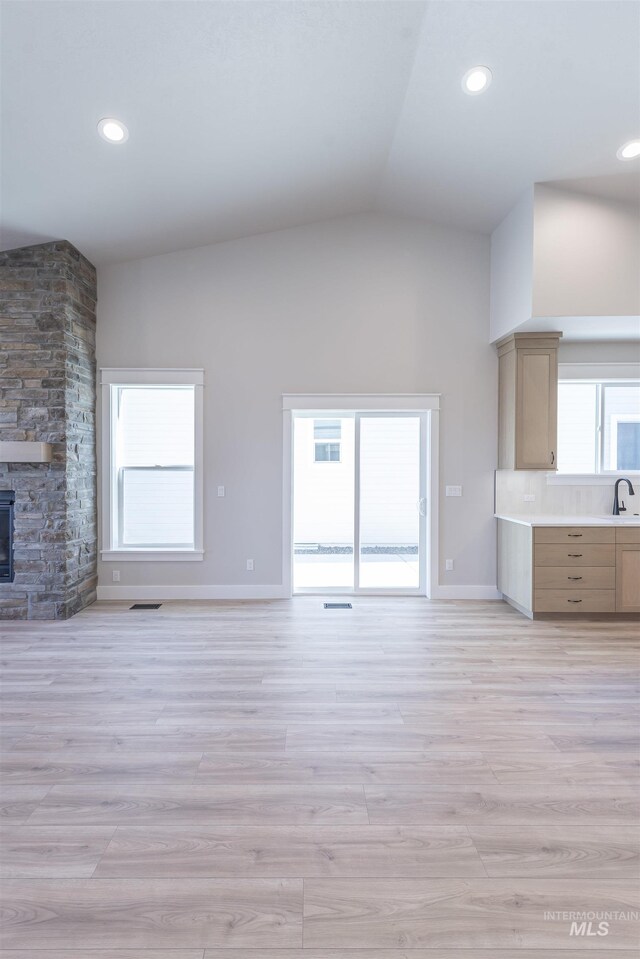 unfurnished living room with high vaulted ceiling, a wealth of natural light, a sink, and light wood-style flooring