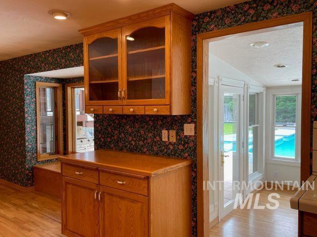 10809 W Cruser, Boise, ID 83709 - kitchen with wallpapered walls, light wood finished floors, brown cabinets, glass insert cabinets, and vaulted ceiling