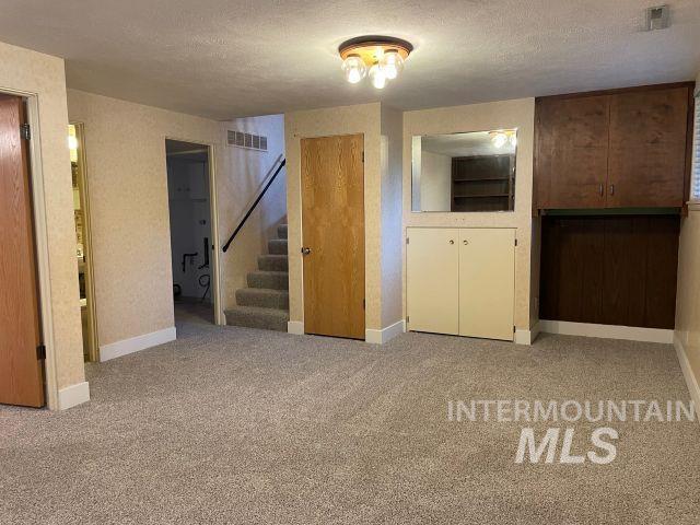 10809 W Cruser, Boise, ID 83709 - unfurnished living room featuring stairway, baseboards, carpet flooring, and a textured ceiling