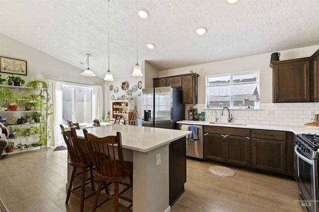 kitchen with sink, hanging light fixtures, appliances with stainless steel finishes, a kitchen island, and backsplash