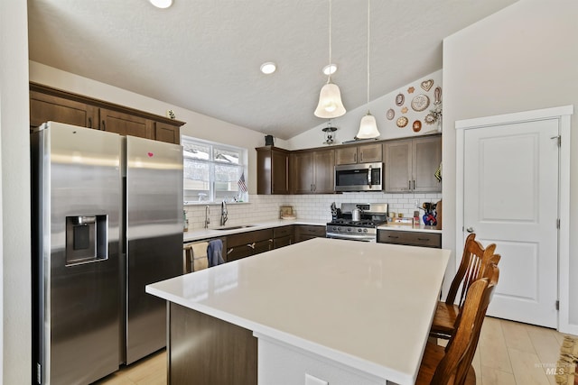 kitchen featuring dark brown cabinetry, sink, hanging light fixtures, a kitchen island, and stainless steel appliances