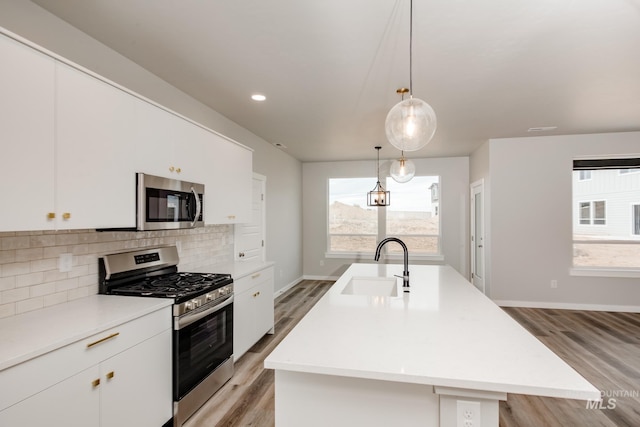 kitchen with white cabinetry, sink, an island with sink, light hardwood / wood-style floors, and appliances with stainless steel finishes