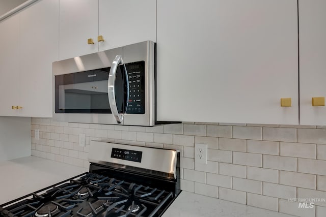 kitchen featuring backsplash, light stone counters, white cabinetry, and stainless steel appliances