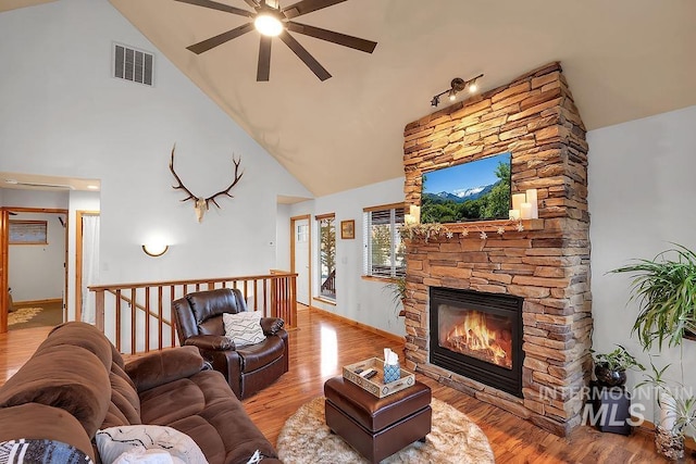 living room featuring a stone fireplace, light wood-type flooring, and high vaulted ceiling