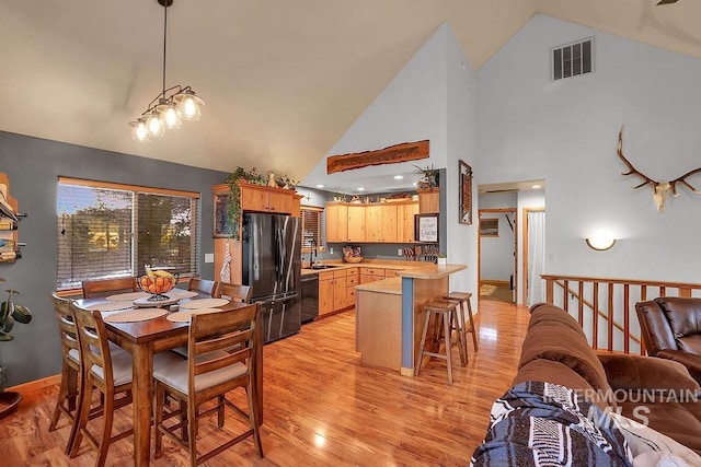 dining space with light hardwood / wood-style flooring, high vaulted ceiling, an inviting chandelier, and sink