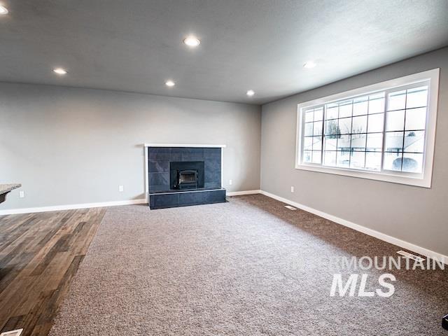 unfurnished living room with baseboards, recessed lighting, a fireplace, and wood finished floors