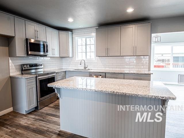 kitchen with appliances with stainless steel finishes, a sink, gray cabinetry, light stone counters, and dark wood-type flooring