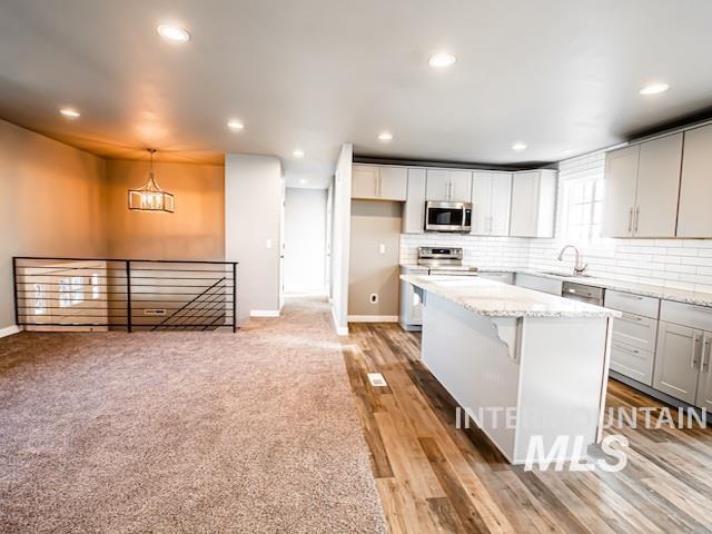 kitchen with stainless steel appliances, baseboards, tasteful backsplash, a kitchen island, and light stone counters
