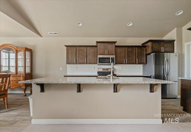 2510 Duchess Trl, Emmett, ID 83617 - kitchen with stainless steel appliances, light stone counters, dark brown cabinetry, a breakfast bar, and vaulted ceiling