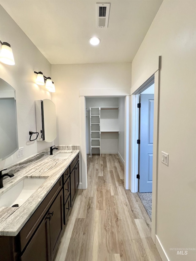 bathroom with visible vents, wood finished floors, a sink, and a spacious closet