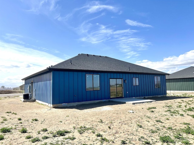 rear view of property featuring board and batten siding, a patio area, roof with shingles, and central AC